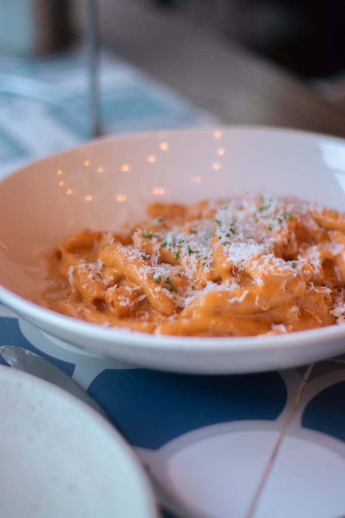 Close-up of creamy pasta in white bowl, topped with grated parmesan.