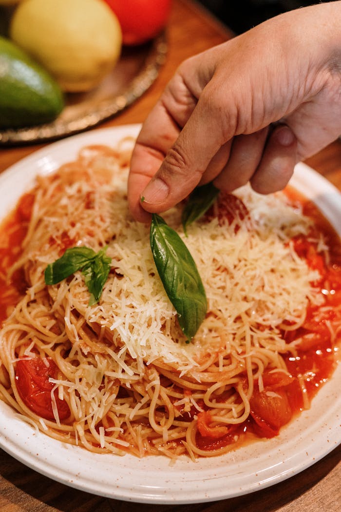 Hand garnishing delicious spaghetti with fresh basil leaves for an authentic Italian touch.